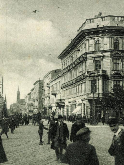 Schwarz-Weiß-Bild eines Gebäudes am Freiheitsplatz in Lodz. Auf dem Platz sind mehrere Menschen zu sehen, die den Platz kreuzen. 