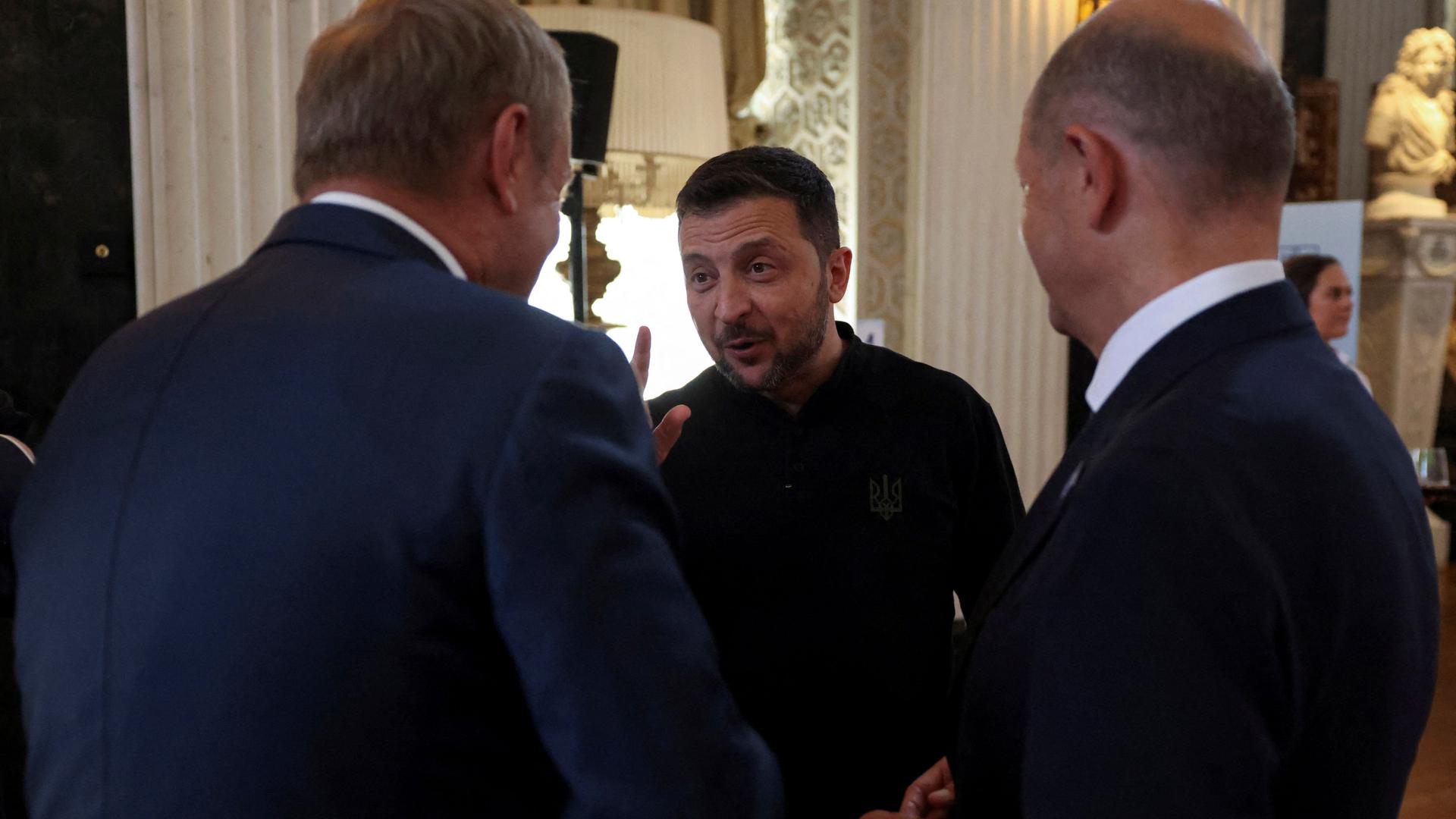 Der ukrainische Präsident Selenskyj spricht mit Polens Ministerpräsident Tusk und Bundeskanzler Scholz. Er steht zwischen den beiden Männern und gestikuliert mit einer Hand.