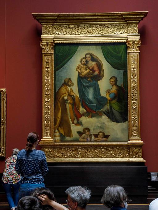 Museumsbesucher- und besucherinnen betrachten die Sixtinische Madonna von Raffael in der Gemäldegalerie Alte Meister in Dresden.