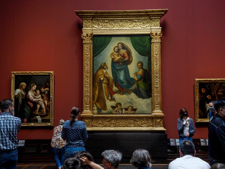Museumsbesucher- und besucherinnen betrachten die Sixtinische Madonna von Raffael in der Gemäldegalerie Alte Meister in Dresden.