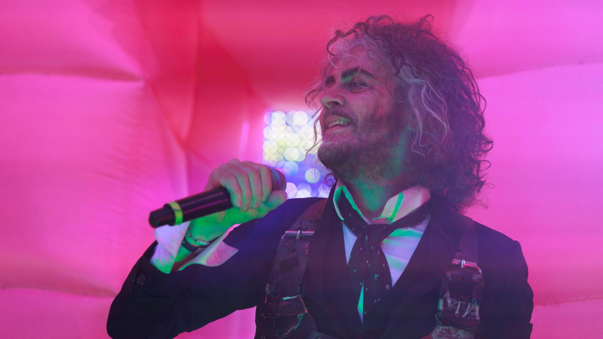 Wayne Coyne von den The Flaming Lips Rock steht auf der Bühne und singt vor einem pinken Hintergrund (beim Granfalloon Festival 2023 in Bloomington, Indiana)