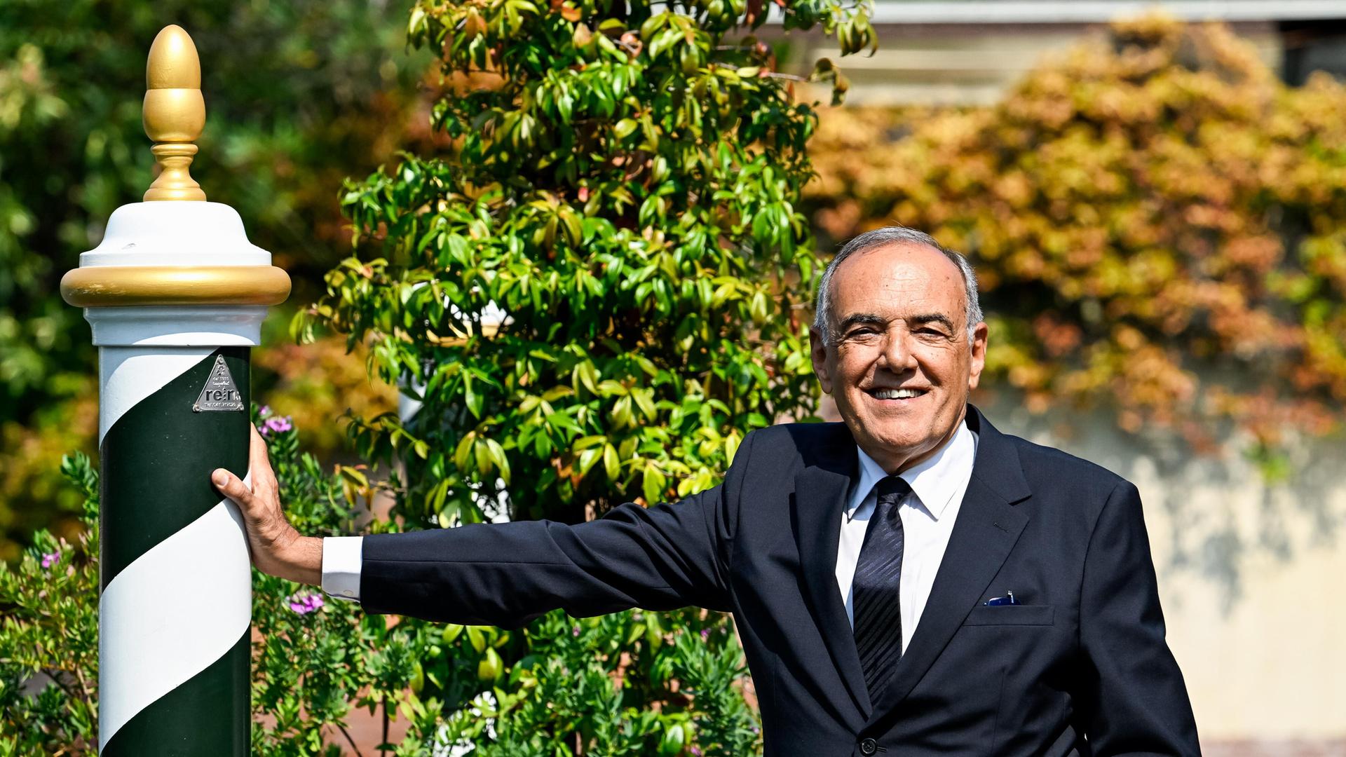 Der Direktor des Filmfests Venedig, Alberto Barbera, steht im Anzug in einem Garten und lehnt sich mit seinem Arm an einen schwarz-weißen Pfahl . Der Direktor des Filmfests Venedig, Alberto Barbera, steht im Anzug in einem Garten und lehnt sich mit seinem Arm an einen schwarz-weißen Pfahl .