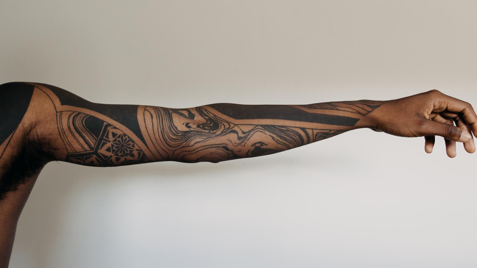 Auf einem ausgestreckten Arm ist eine schwarze Tätowierung mit abstrakten Flächen und Formen zu sehen Auf einem ausgestreckten Arm ist eine schwarze Tätowierung mit abstrakten Flächen und Formen zu sehen