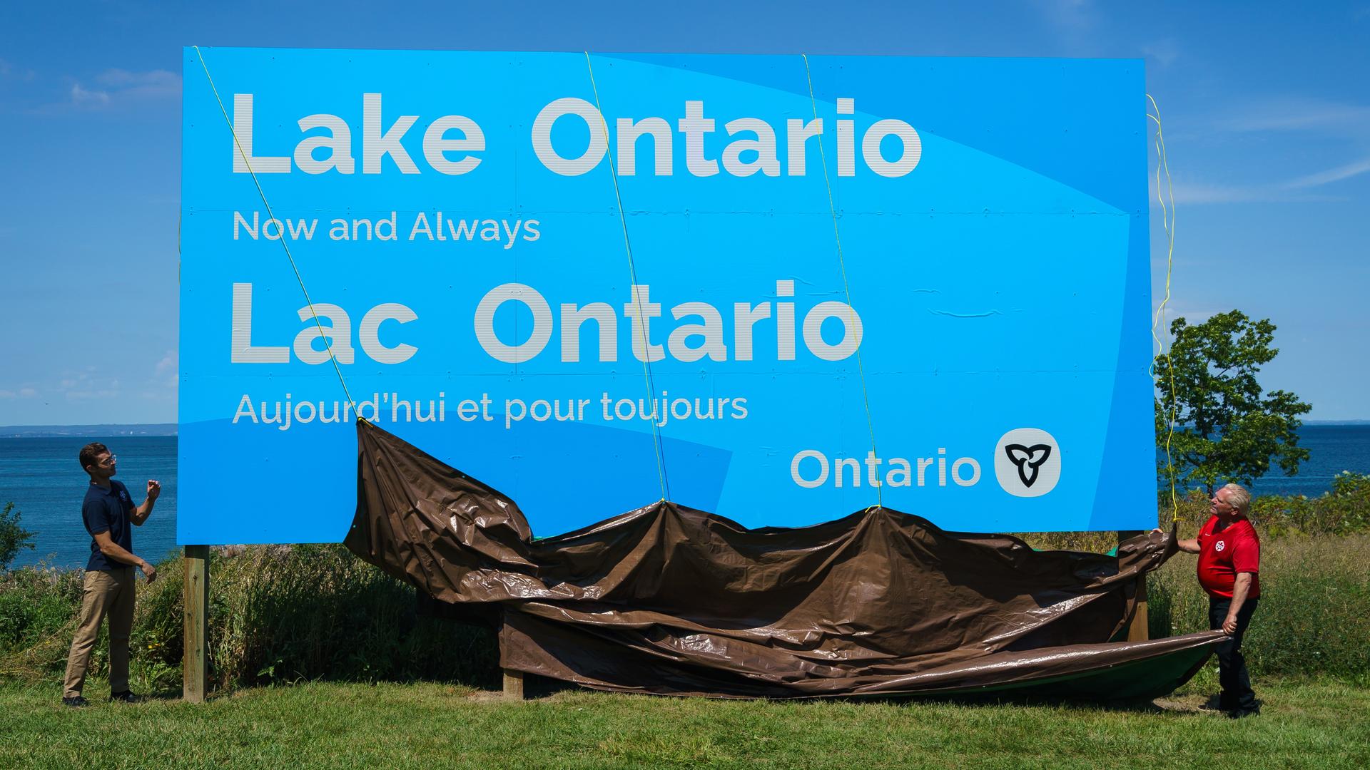 Der Premier-Minister von Ontario enthüllt ein Schild für den Ontario-See. Darauf steht in Englisch und Französisch: "Ontario-See - jetzt und für immer." Der Premier-Minister von Ontario enthüllt ein Schild für den Ontario-See. Darauf steht in Englisch und Französisch: "Ontario-See - jetzt und für immer."
