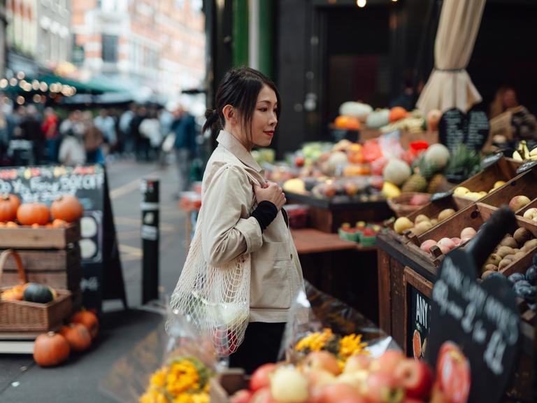 Eine Frau mit einem Einkaufsnetz an der Gemüseauslage eines Wochenmarktstands