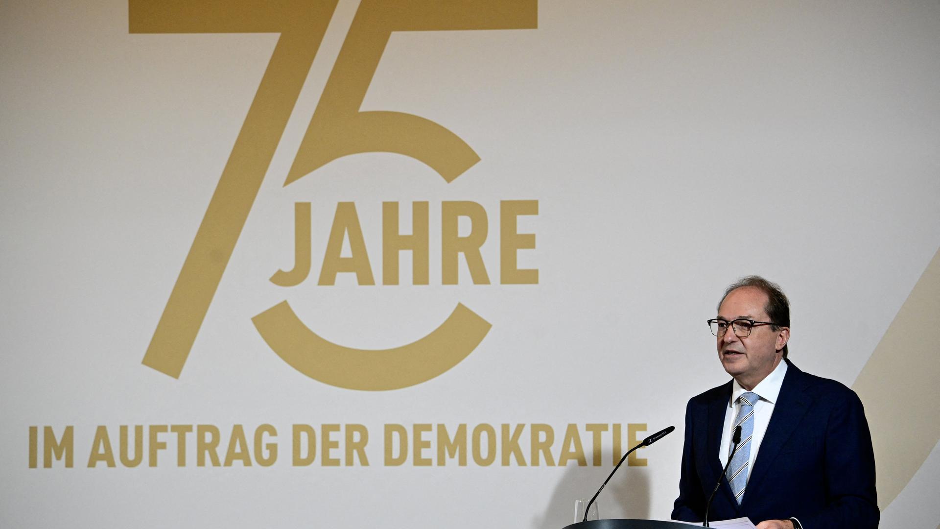 Innenminister Dobrindt steht bei seiner Rede anläßlich des 75. Jahrestages der Gründung des Verfassungsschutzes hinter einem Rednerpult. Hinter ihm an der Wand steht "75 Jahre im Auftrag der Demokratie".