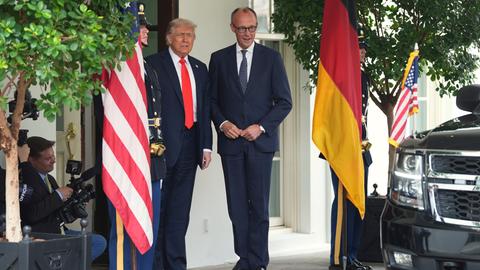 Bundeskanzler Merz und US-Präsident Trump stehen nebeneinander vor dem Weißen Haus. Neben ihnen hängen jeweils die Landesfahnen.