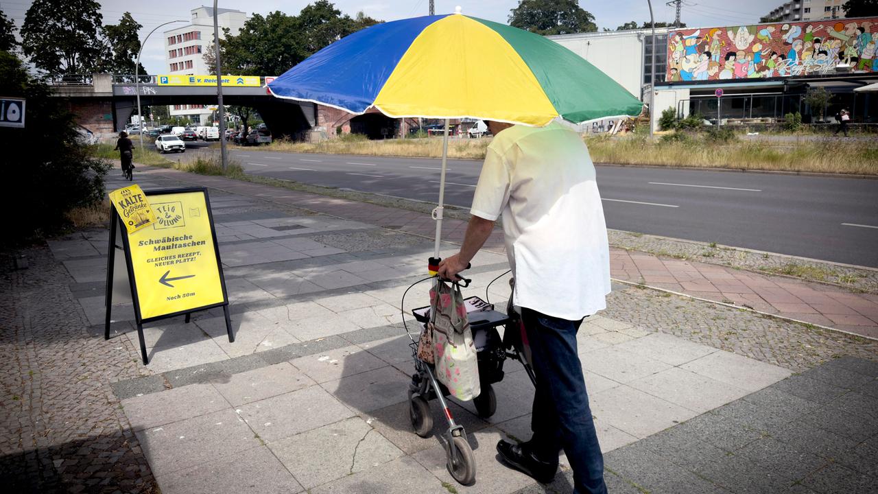 Alter Mann mit Rolator schützt sich vor der Sonne und Hitze mit einem großen Sonnenschirm in Berlin Deutschland.
