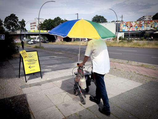 Alter Mann mit Rolator schützt sich vor der Sonne und Hitze mit einem großen Sonnenschirm in Berlin Deutschland. Alter Mann mit Rolator schützt sich vor der Sonne und Hitze mit einem großen Sonnenschirm in Berlin Deutschland.