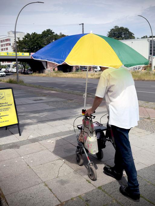 Alter Mann mit Rolator schützt sich vor der Sonne und Hitze mit einem großen Sonnenschirm in Berlin Deutschland. Alter Mann mit Rolator schützt sich vor der Sonne und Hitze mit einem großen Sonnenschirm in Berlin Deutschland.