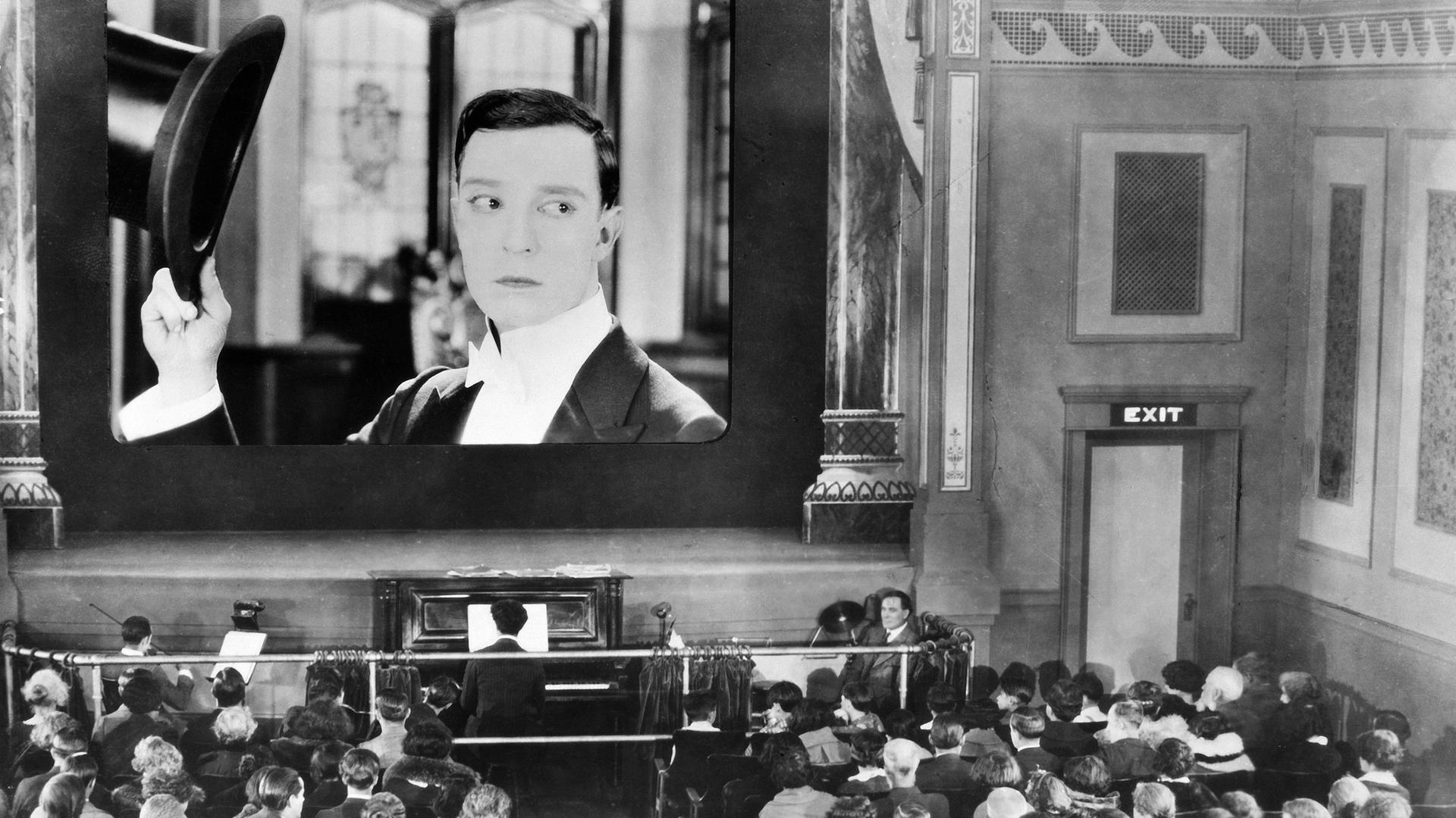 Schwarz-Weiß-Foto eines voll besetzten Kinos in New York im Jahr 1925, das einen Stummfilm mit Buster Keaton zeigt. Dazu spielt ein Klavierspieler.