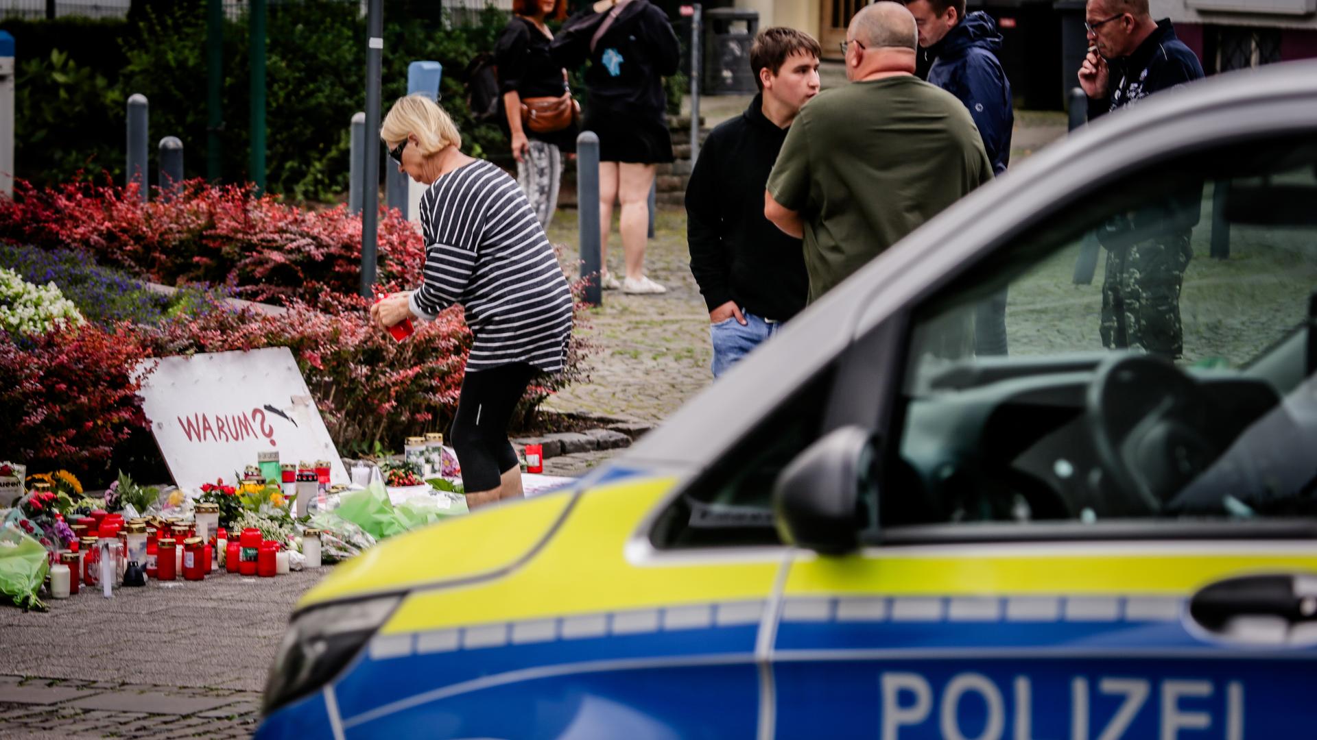 Nach dem Messerangriff von Solingen legen Menschen Blumen und Kerzen nieder. Im Vordergrund steht ein Polizeiauto. 