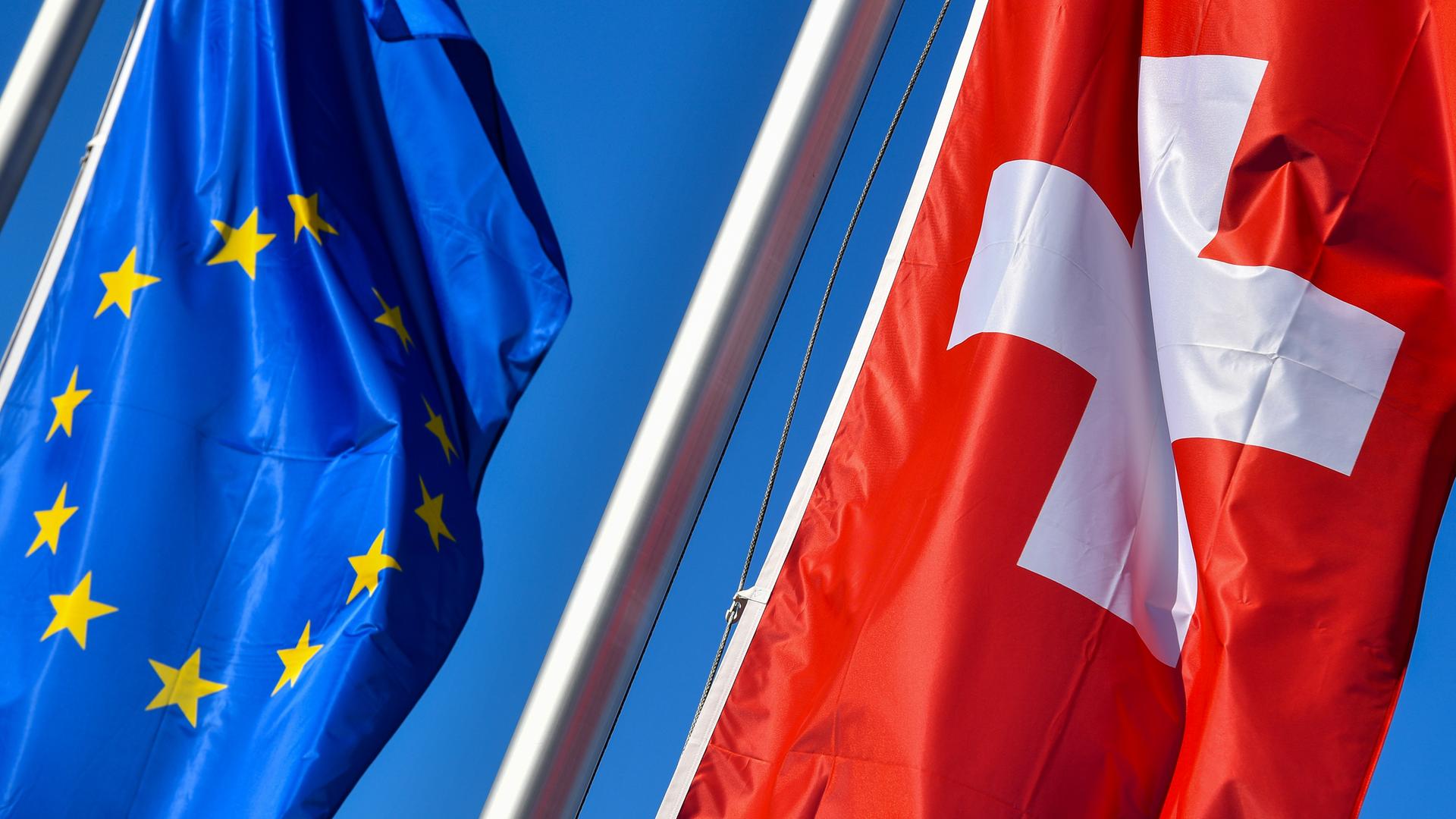 Die Nationalflagge der Schweiz (rechts) weht neben der Flagge der EU vor blauem Himmel.
