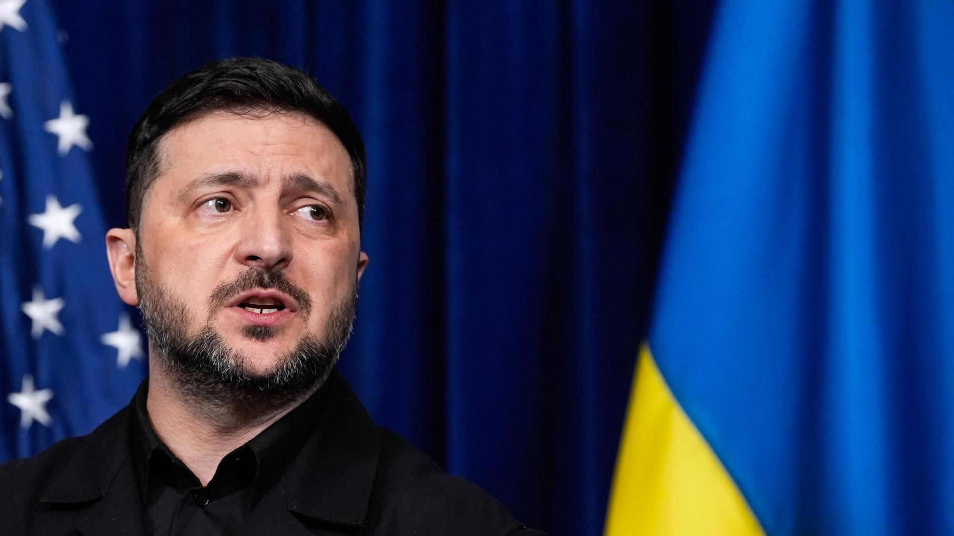 Wolodymyr Selensky spricht während einer Pressekonferenz, dahinter zu sehen sind eine amerikanische und eine ukrainische Flagge.