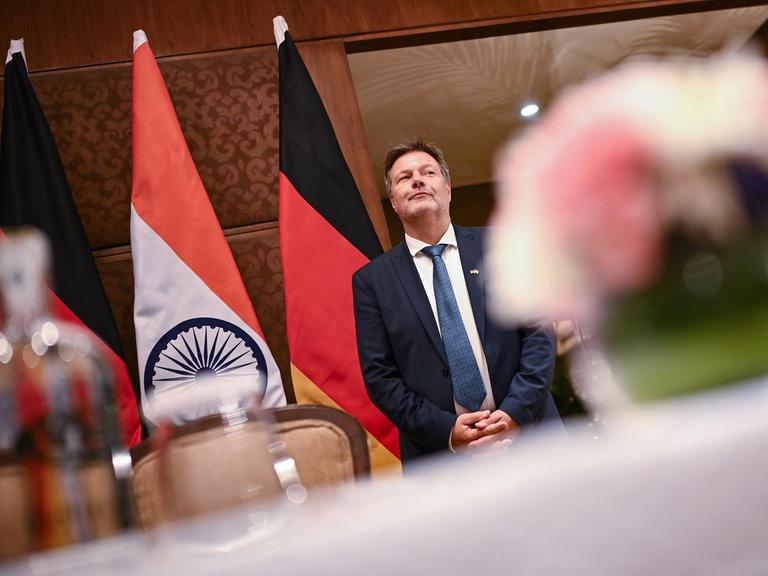 Robert Habeck steht wartend vor deutschen und indischen Nationalflaggen.