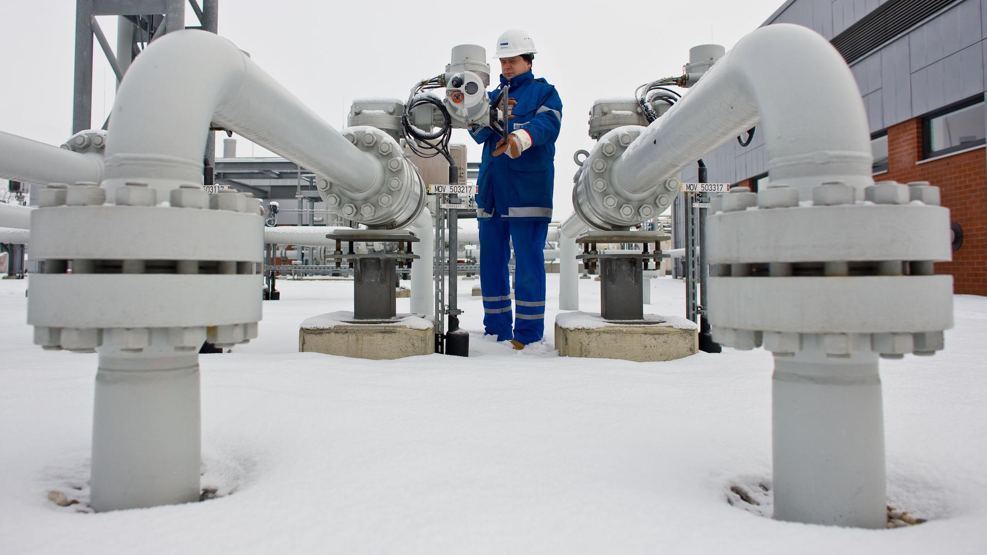Eine Person im Blaumann kontrolliert die verschneiten Rohre eines Erdgasspeichers.