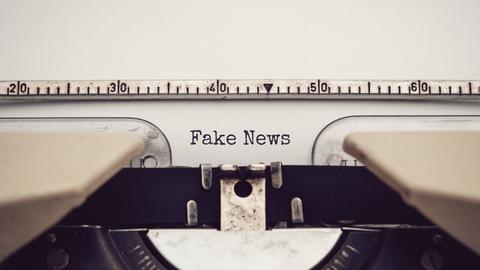 Nahaufnahme einer analagen Schreibmaschine, mit der die Wörter "Fake News" auf ein eingespanntes Blatt Papier getippt wurden.