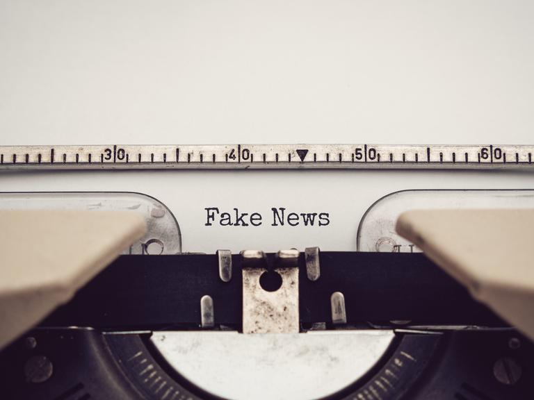 Nahaufnahme einer analagen Schreibmaschine, mit der die Wörter "Fake News" auf ein eingespanntes Blatt Papier getippt wurden.