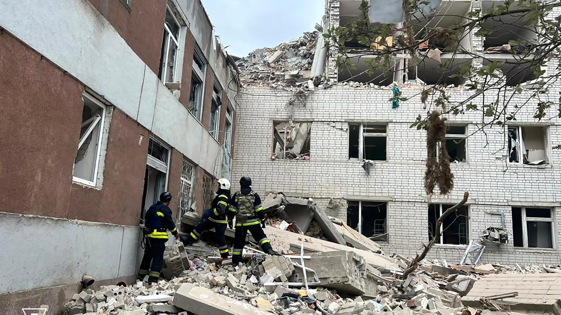 Auf diesem vom ukrainischen Katastrophenschutz zur Verfügung gestellten Foto arbeiten Rettungskräfte am Ort eines russischen Raketeneinschlags in Tschernihiw. Sie stehen auf Trümmern, im Hintergrund ist ein zerstörtes Gebäude.