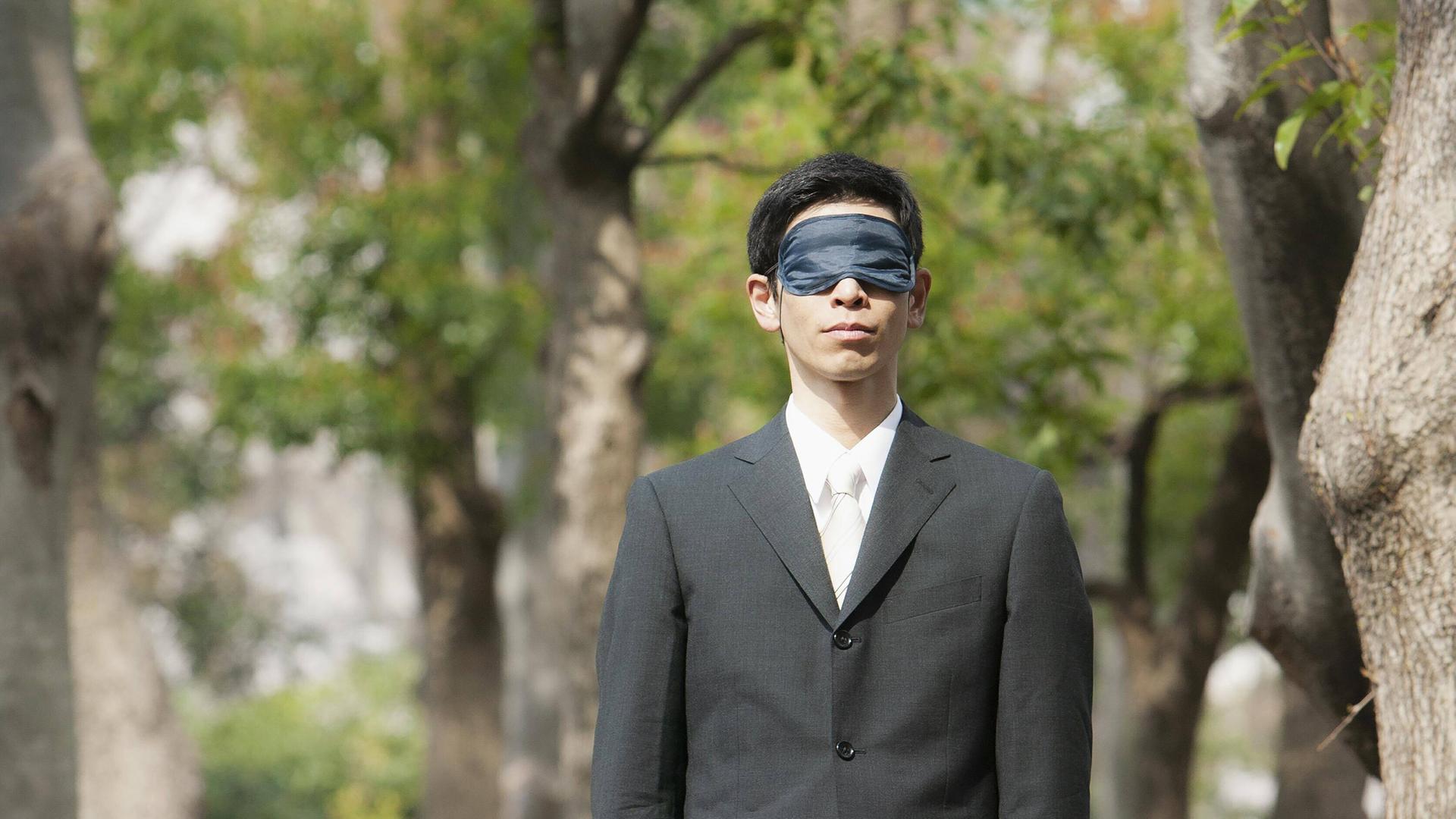 Ein Mann mit Augenmaske steht in einem Park.