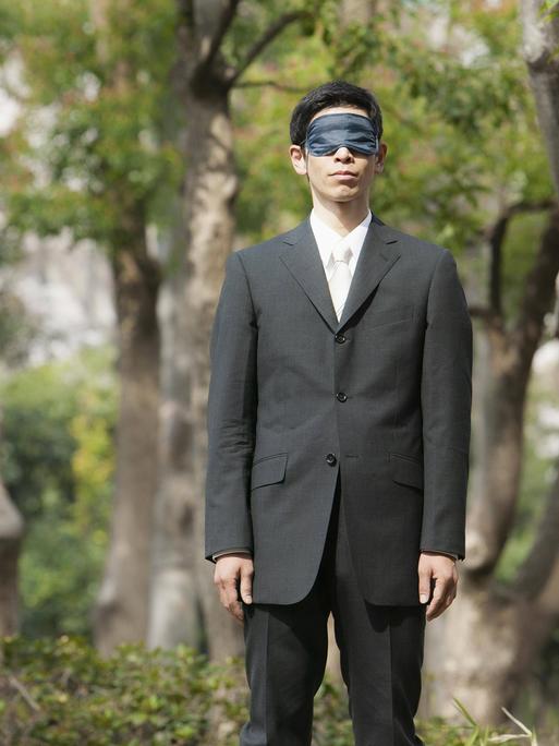 Ein Mann mit Augenmaske steht in einem Park.