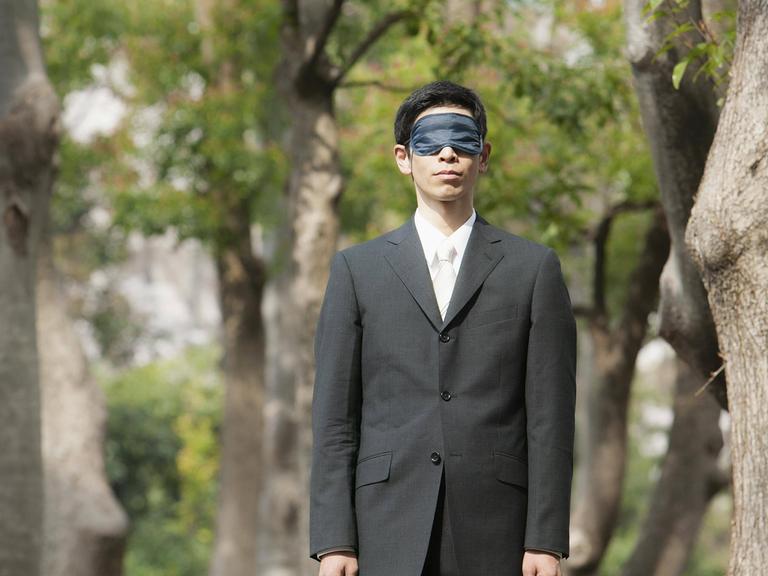Ein Mann mit Augenmaske steht in einem Park.
