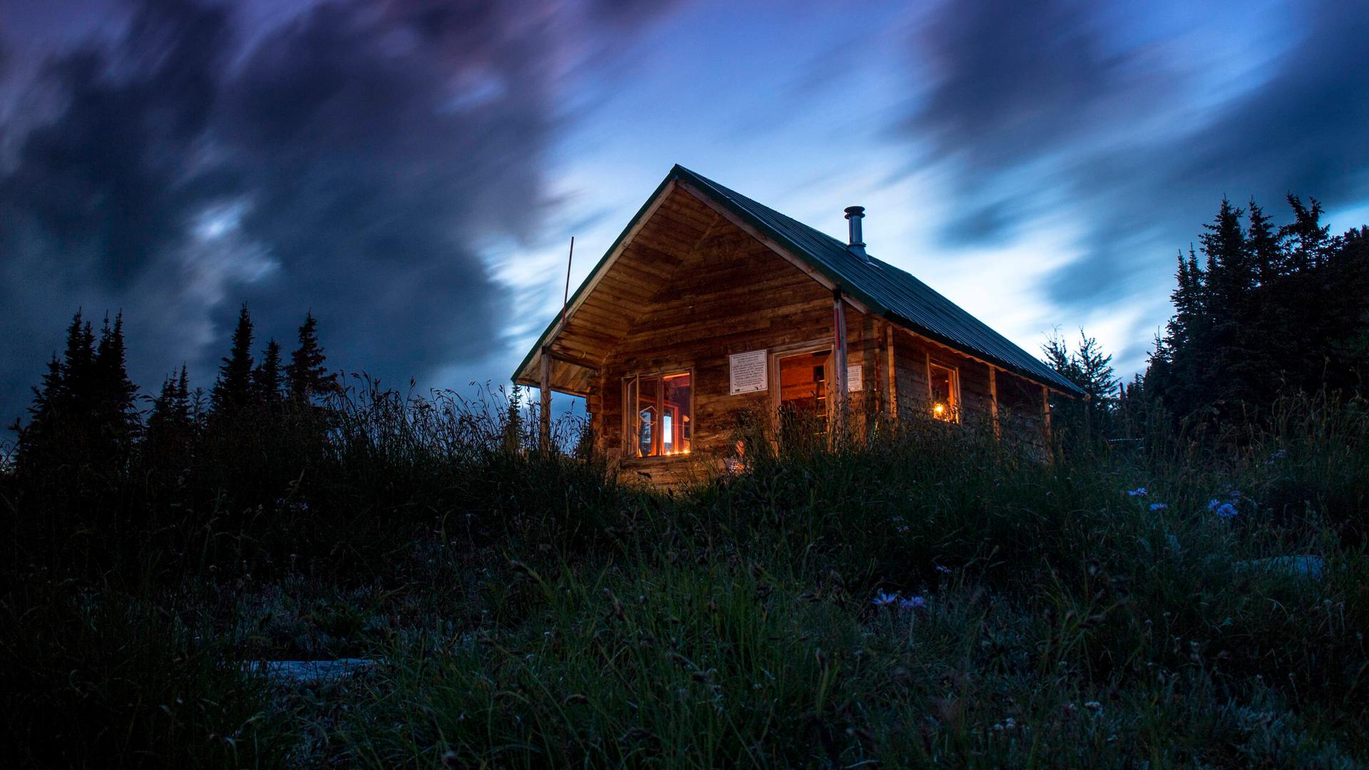 Ein Haus an einem Berg in der Dunkelheit. Drinnen brennen einzelne Lichter.