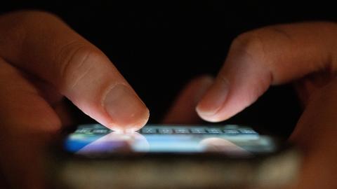 Zwei Finger tippen auf einem blau leuchtenden Smartphone. Zwei Finger tippen auf einem blau leuchtenden Smartphone.