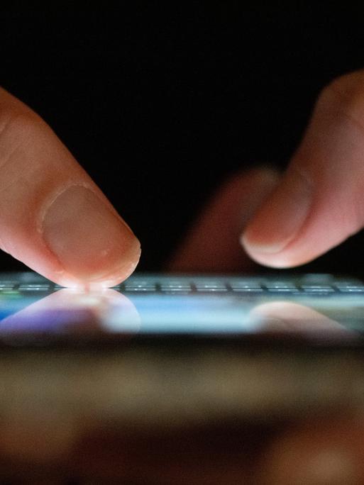 Zwei Finger tippen auf einem blau leuchtenden Smartphone. Zwei Finger tippen auf einem blau leuchtenden Smartphone.