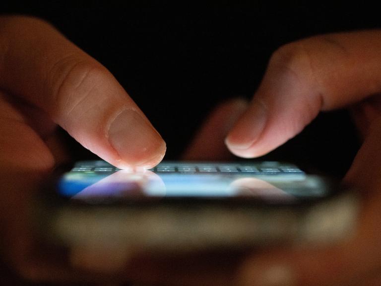 Zwei Finger tippen auf einem blau leuchtenden Smartphone. Zwei Finger tippen auf einem blau leuchtenden Smartphone.