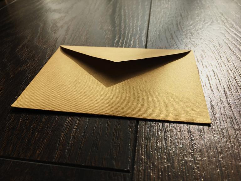 Ein goldener Briefumschlag liegt auf einer Fläche aus Holz.