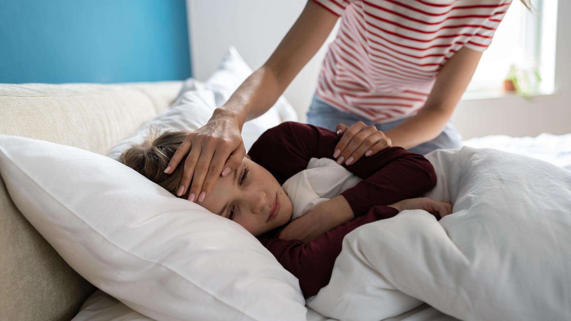 Ein kleiner Junge liegt im Bett, eine Frau fühlt an seiner Stirn die Temperatur