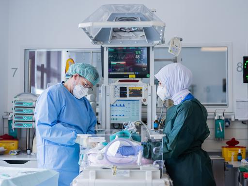Ein Arzt und eine Krankenschwester stehen in Schutzanzug mit Mundschutz an einem Intensivbett auf der Neugeborenenstation.