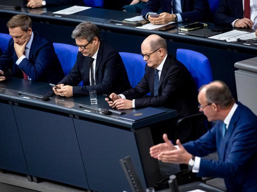 Bundeskanzler Olaf Scholz, Bundeswirtschaftsminister Robert Habeck und Bundesfinanzminister Christian Lindner sitzen in der Regierungsbank im Bundestag und blicken auf ihre Handys.