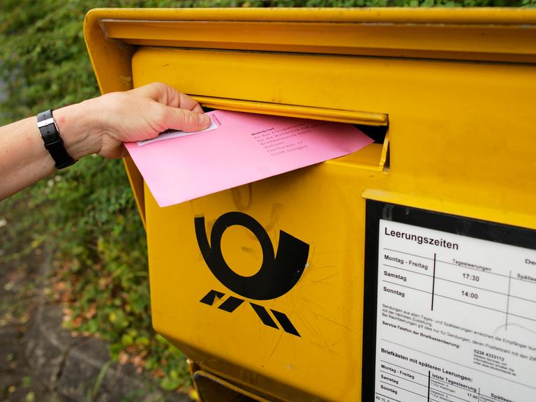 Ein Wahlbrief wird in einen Briefkasten der Deutschen Post gesteckt.
