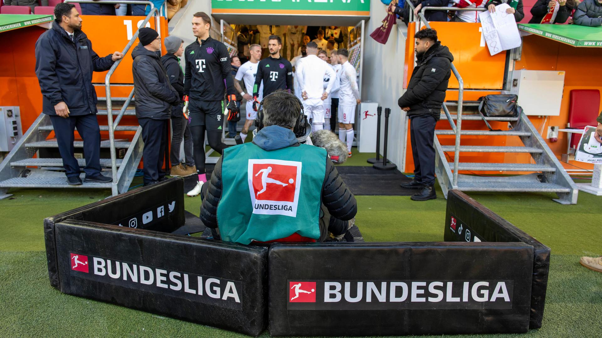 Ein Kameramann verfolgt die Spieler beim Einlauf auf den Rasen aus den Katakomben beim Fußball-Bundesliga-Spiel FC Augsburg - FC Bayern München.