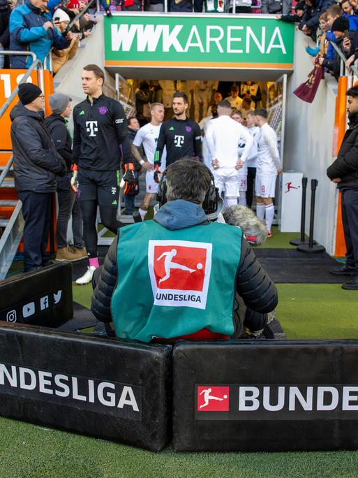Ein Kameramann verfolgt die Spieler beim Einlauf auf den Rasen aus den Katakomben beim Fußball-Bundesliga-Spiel FC Augsburg - FC Bayern München.