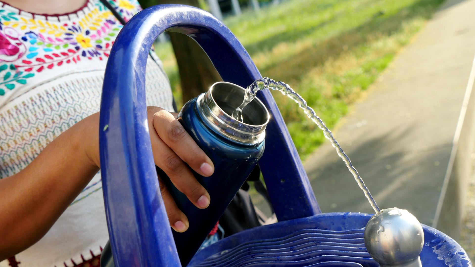Eine Frau füllt sich an einem öffentlichen Trinkbrunnen ihre Wasserflasche auf. 