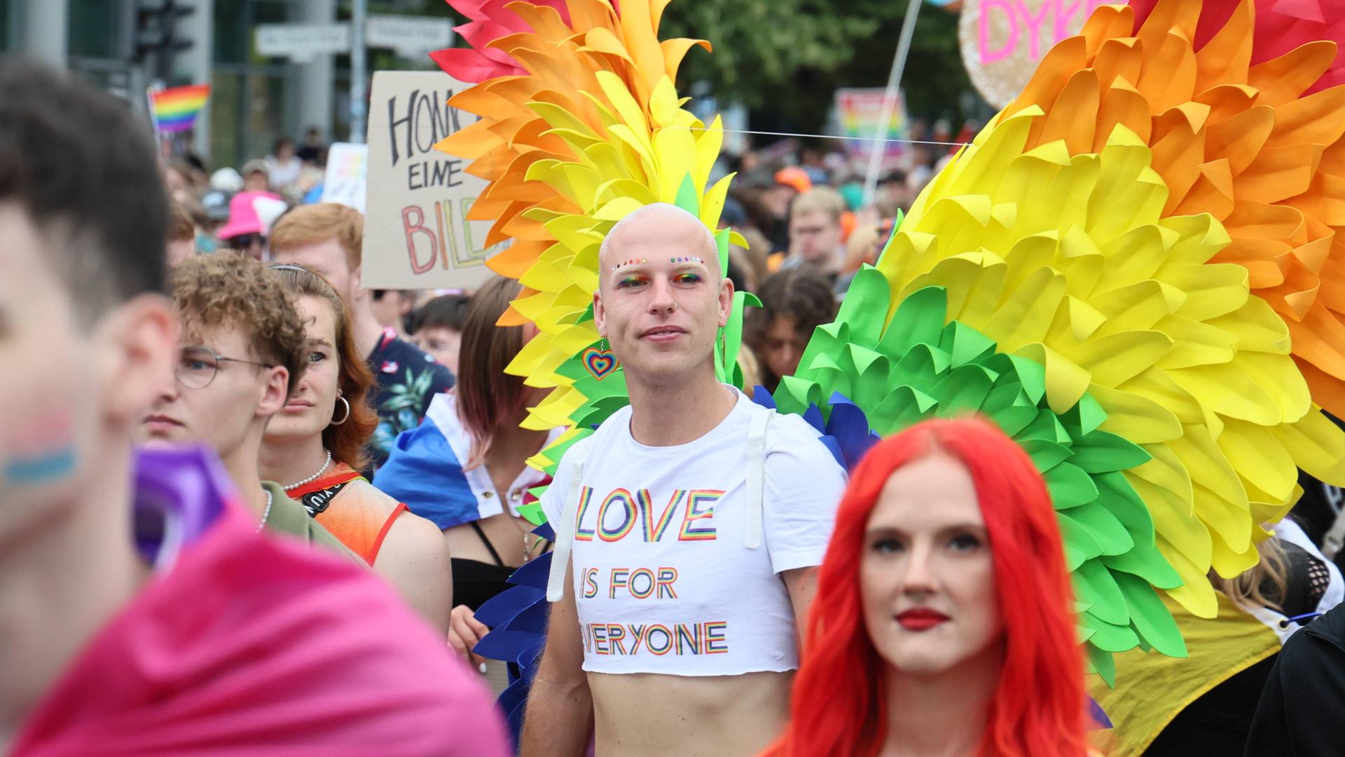 Menschen bei der CSD Demonstration in Berlin. Im Vordergrund eine Frau mit roten Haaren und ein Mann mit Flügeln in Regenbogenfarben. Menschen bei der CSD Demonstration in Berlin. Im Vordergrund eine Frau mit roten Haaren und ein Mann mit Flügeln in Regenbogenfarben.