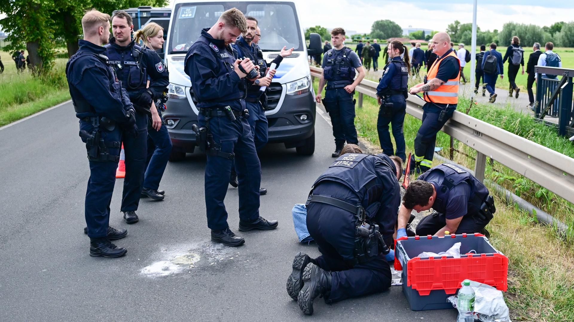 Berlin-Schönefeld: Polizeibeamte lösen während der Internationalen Luft- und Raumfahrtausstellung (ILA) auf dem Berlin ExpoCenter Airport an einer Zufahrtsstraße eine festgeklebte Person. Berlin-Schönefeld: Polizeibeamte lösen während der Internationalen Luft- und Raumfahrtausstellung (ILA) auf dem Berlin ExpoCenter Airport an einer Zufahrtsstraße eine festgeklebte Person.