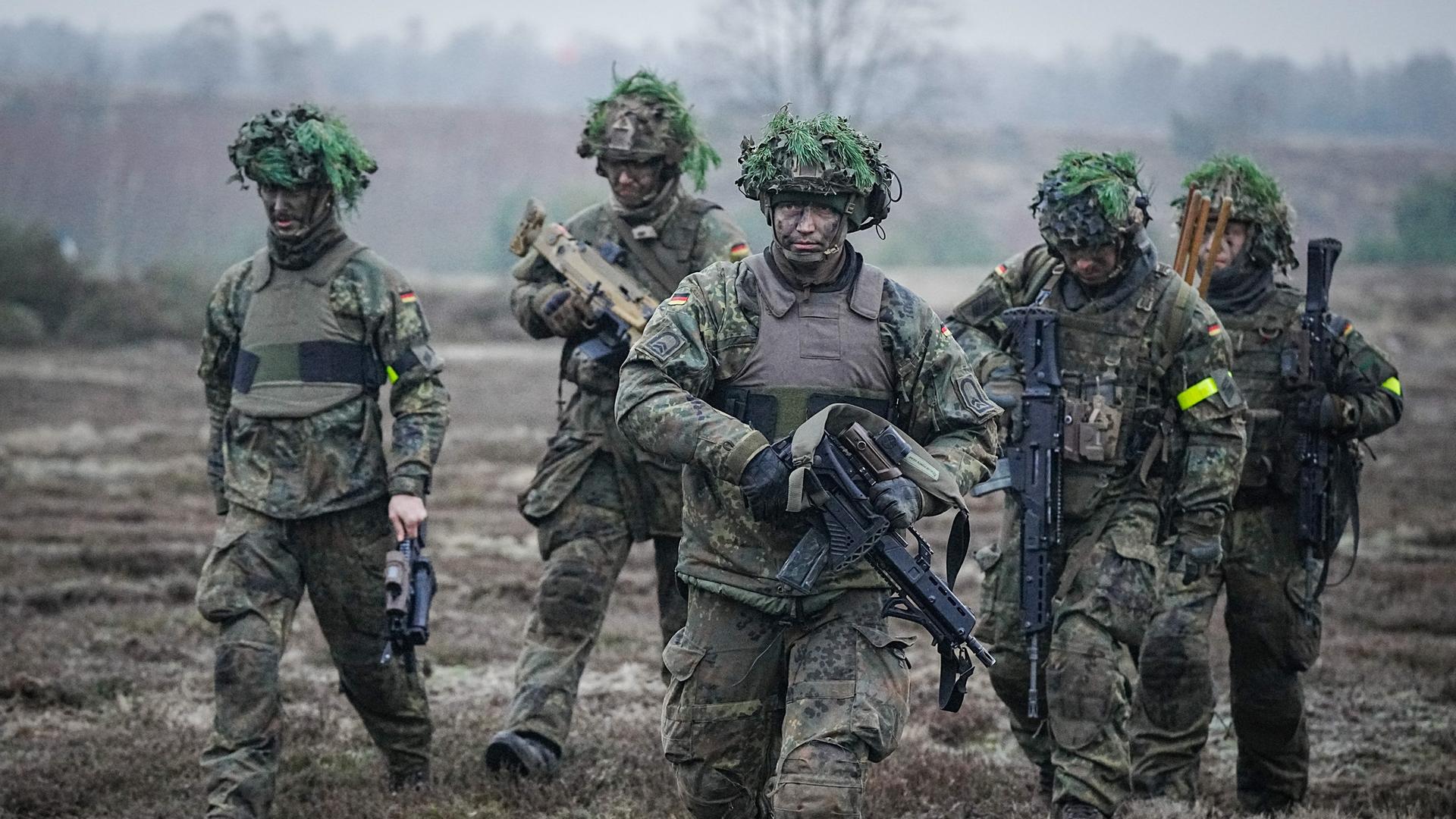 Bundeswehrsoldaten nehmen an einer Übung im Beisein des Verteidigungsministers bei dessen Antrittsbesuch bei der Bundeswehr auf dem Truppenübungsplatz Altengrabow teil. Fünf Soldaten mit Bewaffnung und Kampfmontur gehen durchs Gelände.