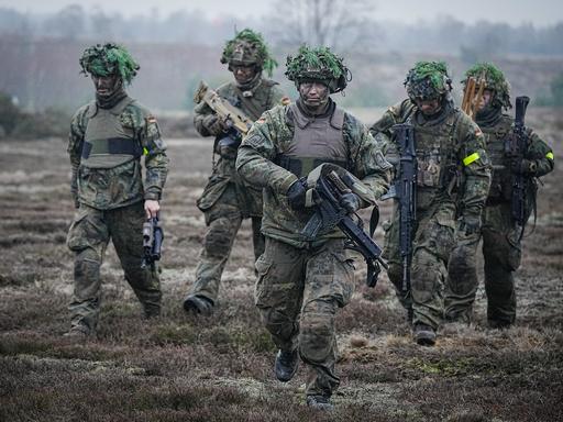 Bundeswehrsoldaten nehmen an einer Übung im Beisein des Verteidigungsministers bei dessen Antrittsbesuch bei der Bundeswehr auf dem Truppenübungsplatz Altengrabow teil. Fünf Soldaten mit Bewaffnung und Kampfmontur gehen durchs Gelände.