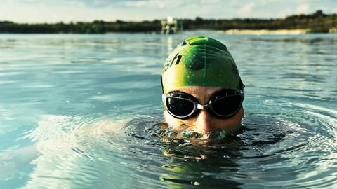 Ein Mann mit grüner Badekappe und dunkler Schwimmbrille schwimmt in einem Seebad durchs Wasser.