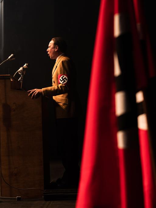Robert Stadlober steht in einer Szene des Films "Führer und Verführer" von Joachim A. Lang als Joseph Goebbels an einem Rednerpult, im Vordergrund ist die Fahne der NSDAP zu sehen.
