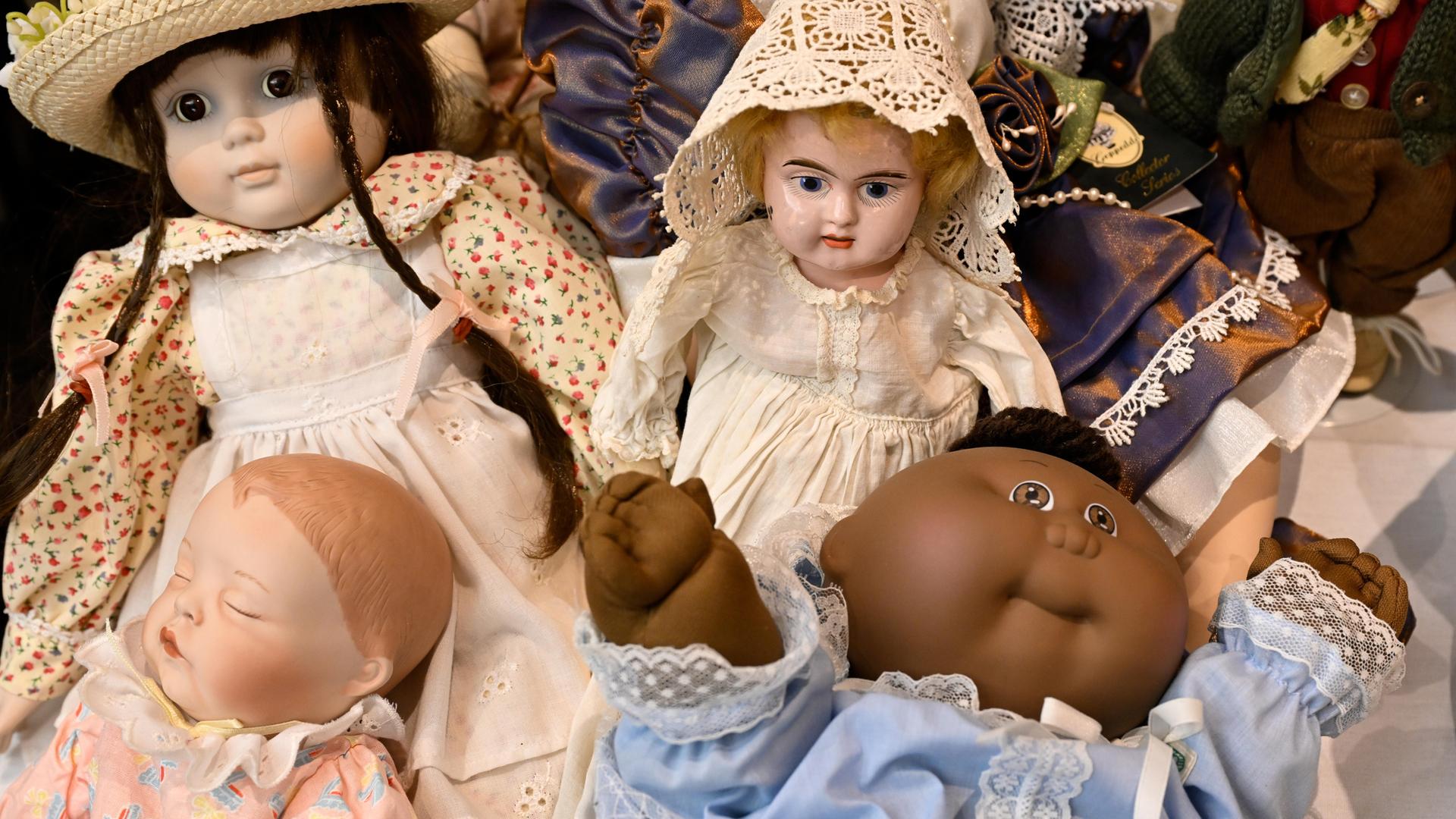 Vier verschiedene Puppen sind auf dem Bild zu sehen, teils mit Porzellangesichtern und feinen Kleidern