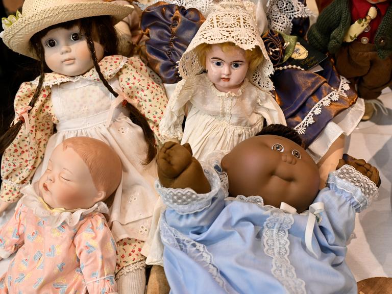 Vier verschiedene Puppen sind auf dem Bild zu sehen, teils mit Porzellangesichtern und feinen Kleidern