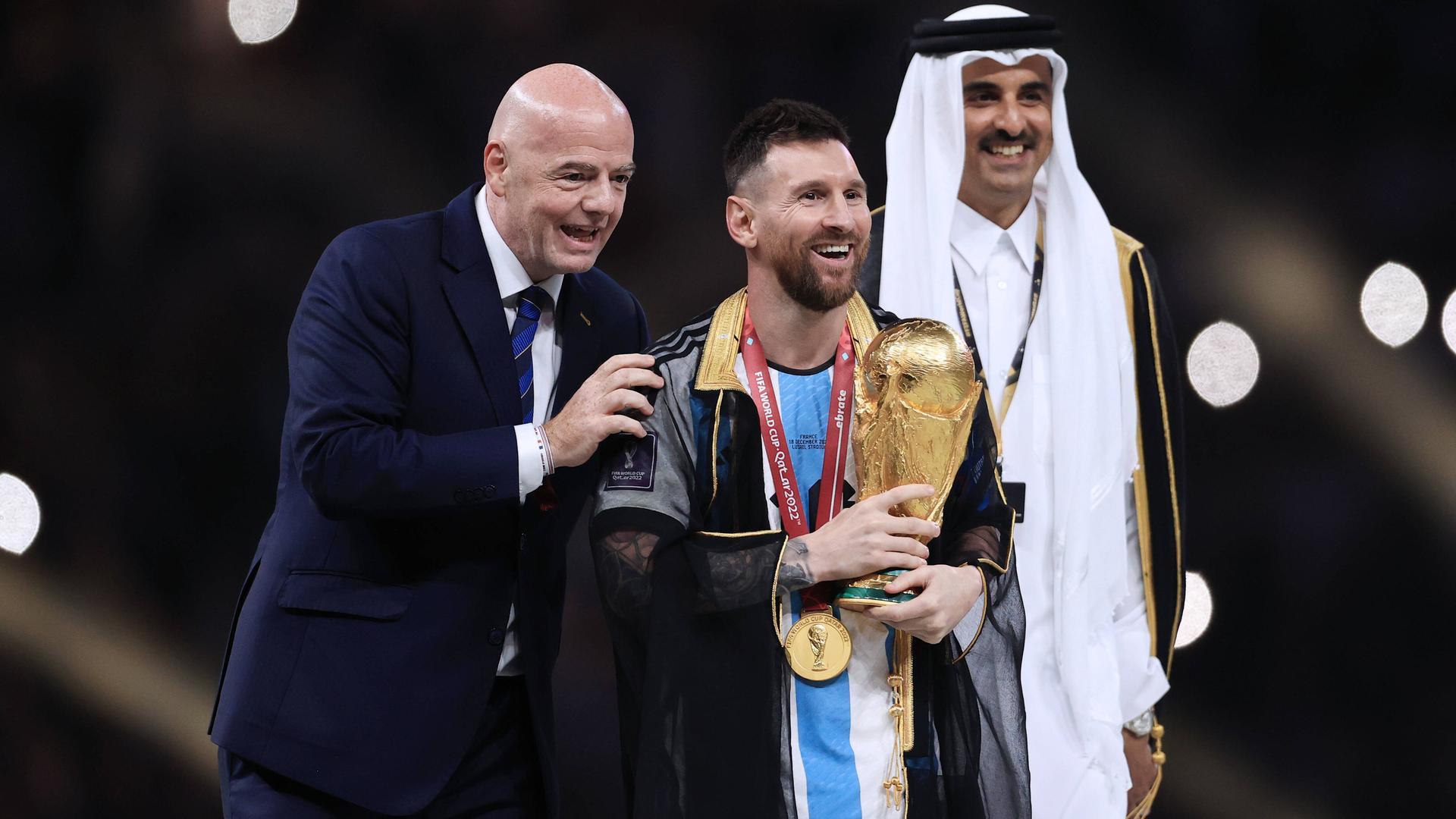 FIFA-Boss Gianni Infantino (l.) überreicht Argentiniens Lionel Messi den WM-Pokal. Rechts daneben steht der Emir von Katar Tamim bin Hamad Al Thani.