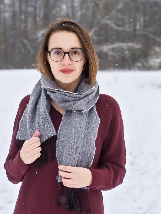 Eine junge Frau mit Schal und Pulli vor verschneiter Landschaft