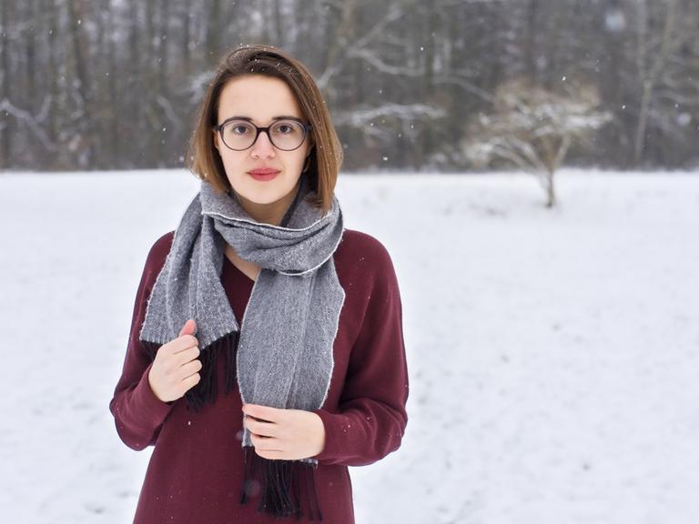 Eine junge Frau mit Schal und Pulli vor verschneiter Landschaft