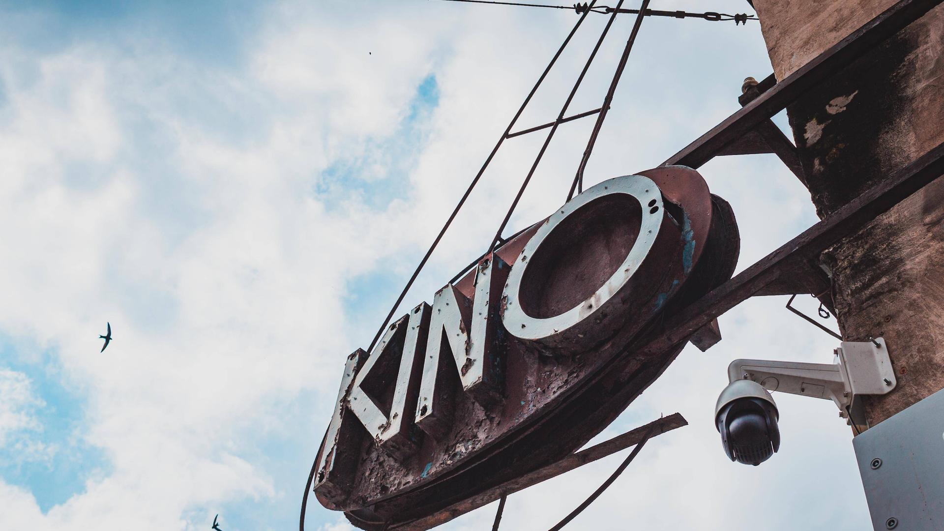 An einem alten Gebäude ist ein Leuchtreklamen-Schild mit der Aufschrift "Kino" angebracht. Es ist in der polnischen Kleinstadt Paczków aufgenommen.